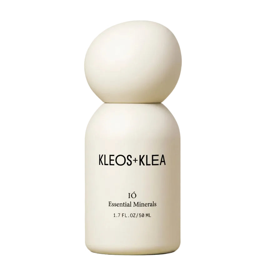 A minimalist white cosmetic bottle with a spherical cap, featuring the brand name 'KLEOS+KLEA' and '10 Essential Minerals' printed on the front, set against a warm beige background.