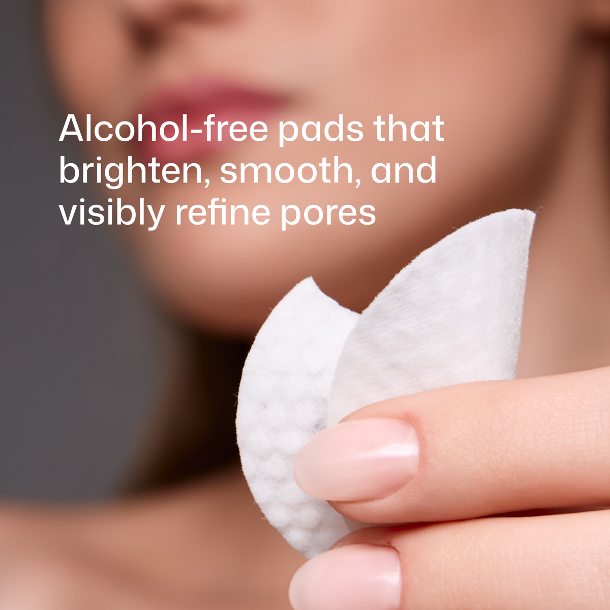 A close-up of a hand holding a white cotton pad, with a blurred face in the background and text that reads: 'Alcohol-free pads that brighten, smooth, and visibly refine pores.'.